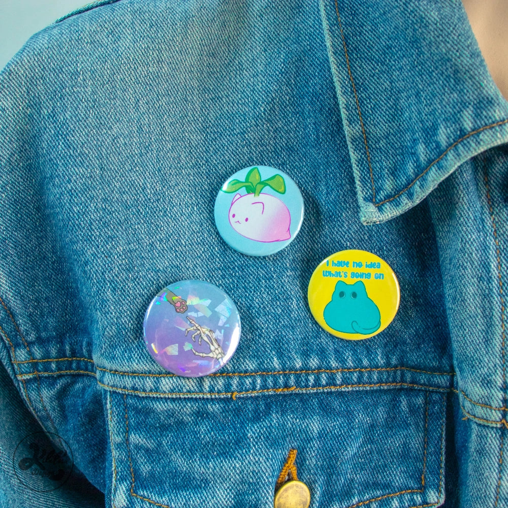 38mm button bin by Kilatora Design. Yellow color with green cat and text "I have no idea what's going on. In the photo, three pins are attached to a denim jacket.
