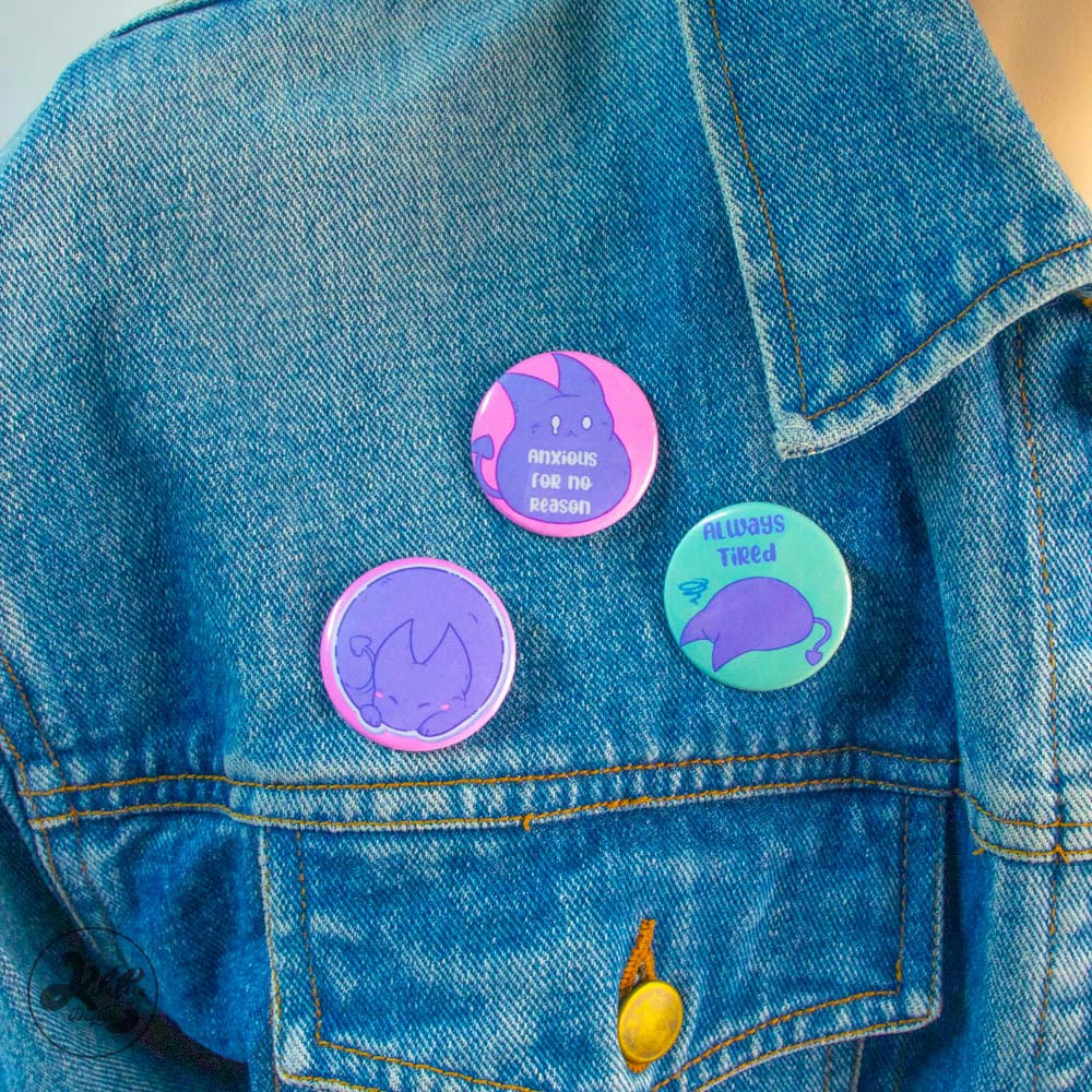 80mm button pin by Kilatora Design. Pink color with purple devil Tora caracter. In the photo, three pins are attached to a denim jacket.