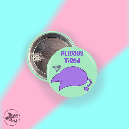 38mm button pin by Kilatora Design. Light green color with purple devil Tora character and text "always tired".