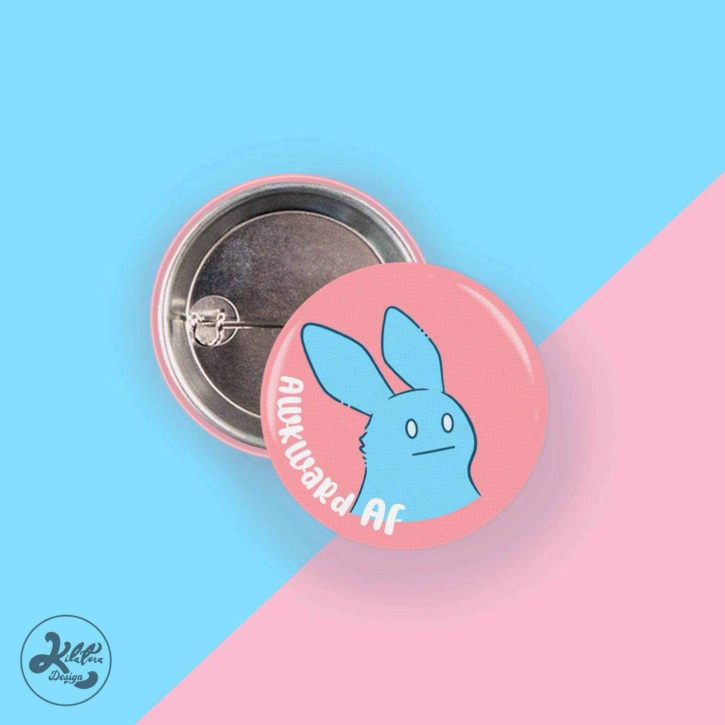 38mm button pin by Kilatora Design. Warm pink color with a blue bunny and text "awkward af".