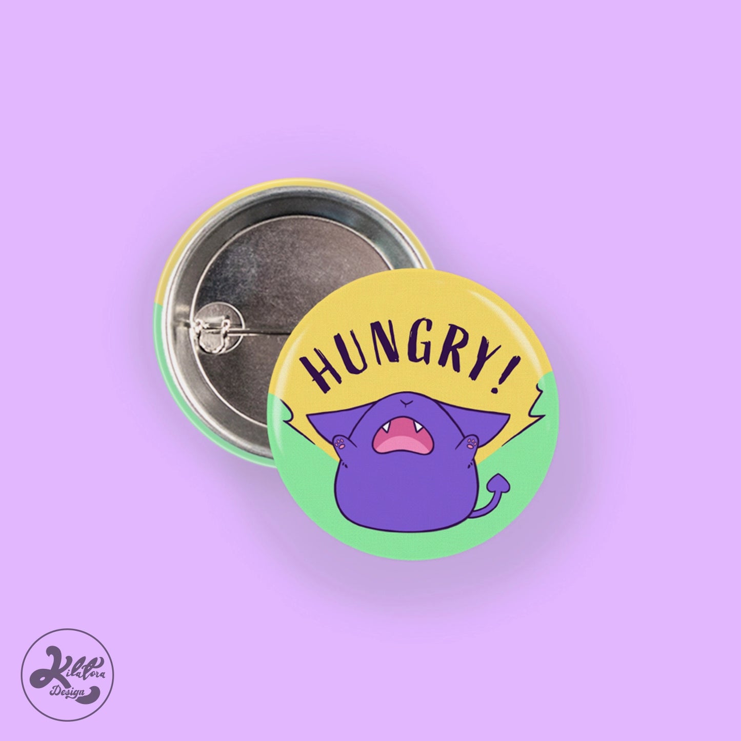 38mm button pin by Kilatora Design. Green pin with purple Tora and text  "hungry".