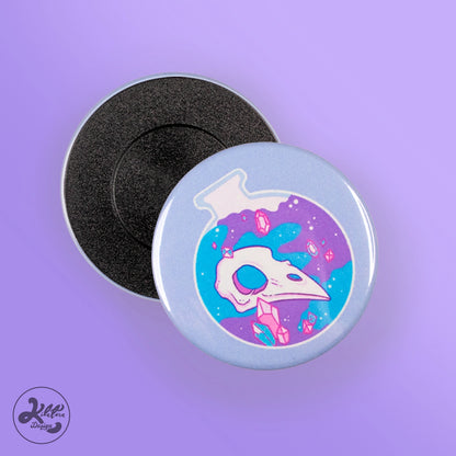 59mm magnet by Kilatora Design. Light blue color with a blue and purple round bottle with a bird's skull and pink crystals inside.